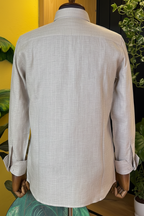 Light gray button-up shirt on a mannequin against a yellow wall with plants.