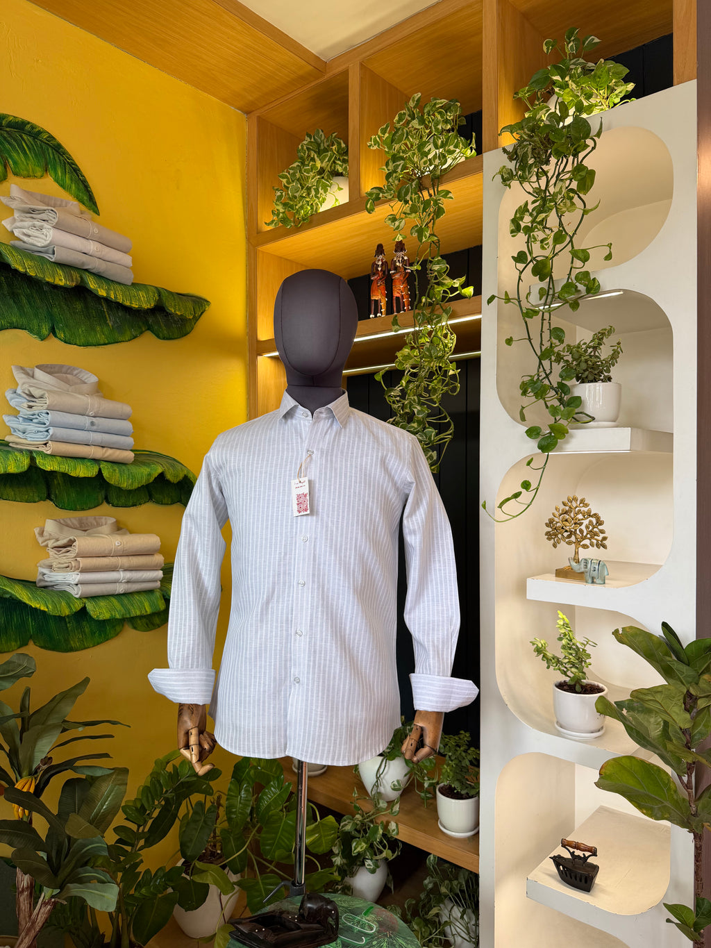Mannequin wearing a striped shirt in a store setting with plants and shelves.